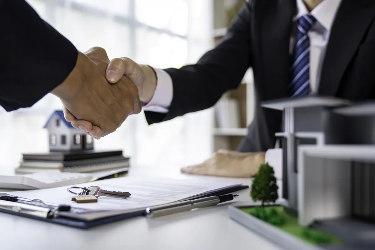Apretón de manos sobre una mesa con contratos y la maqueta de una vivienda
